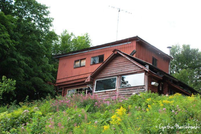 Slider image showing Norm's Cabin prior to the renovation. It's a 2-story red cabin.