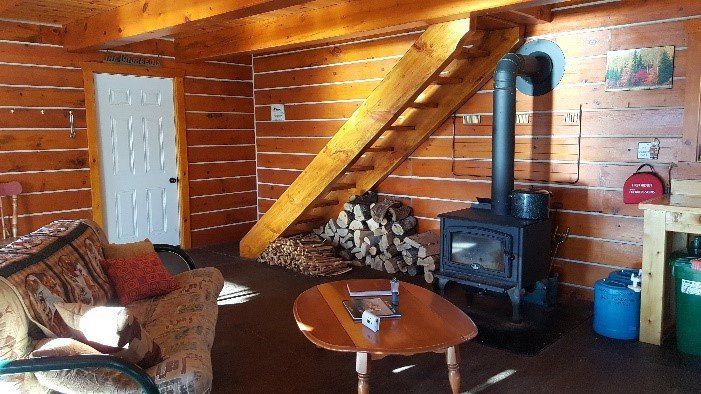 Cozy cabin interior with log walls, wooden staircase, wood-burning stove, and sofa.