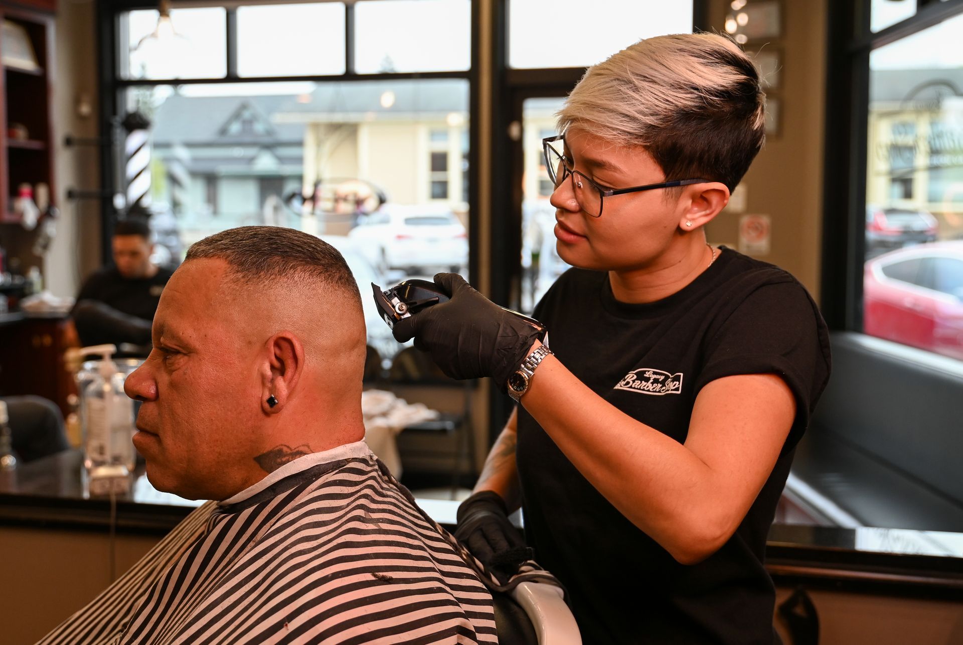 A woman is cutting a man 's hair in a barber shop.