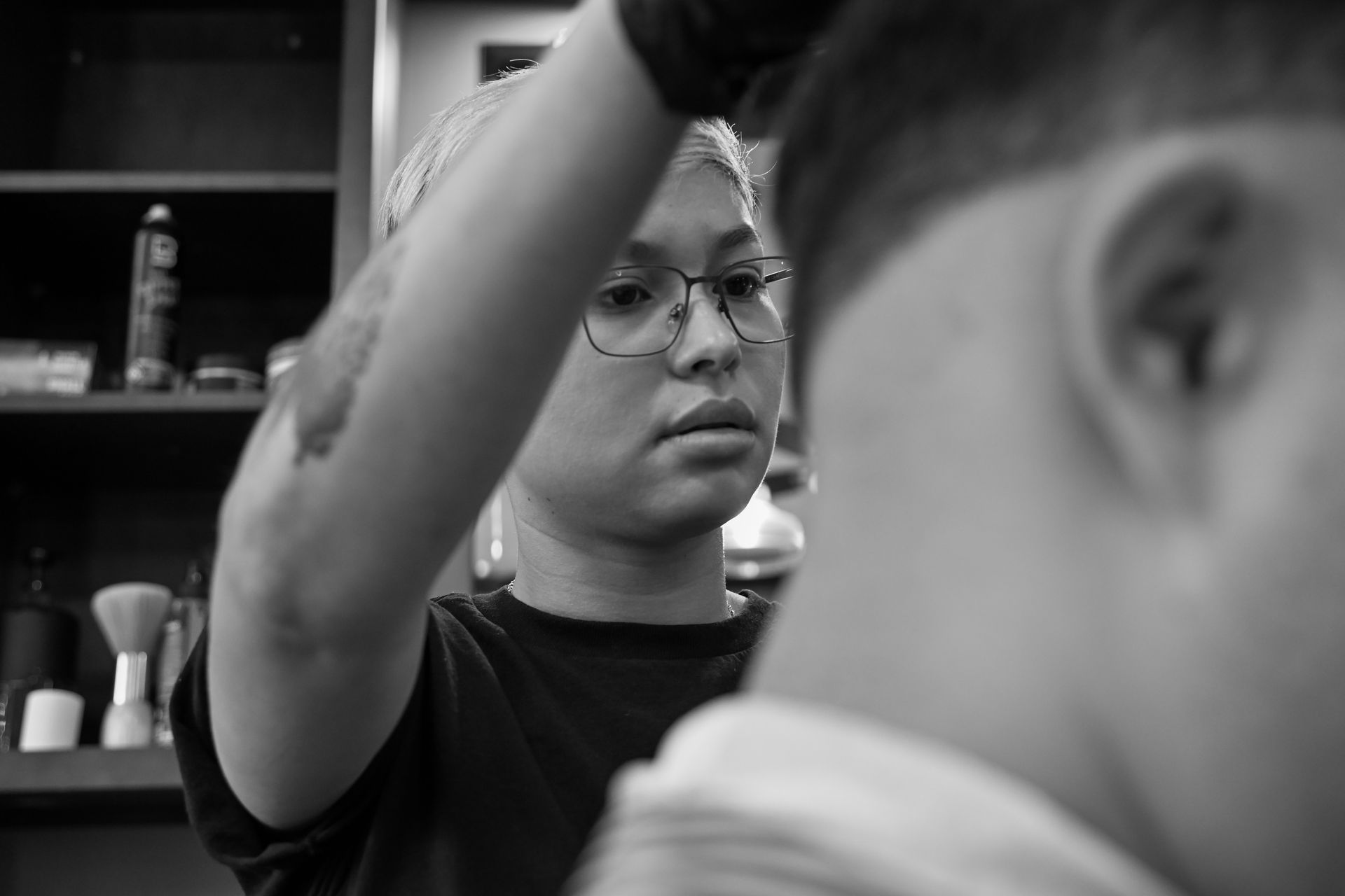 A woman is cutting a man 's hair in a barber shop in a black and white photo.