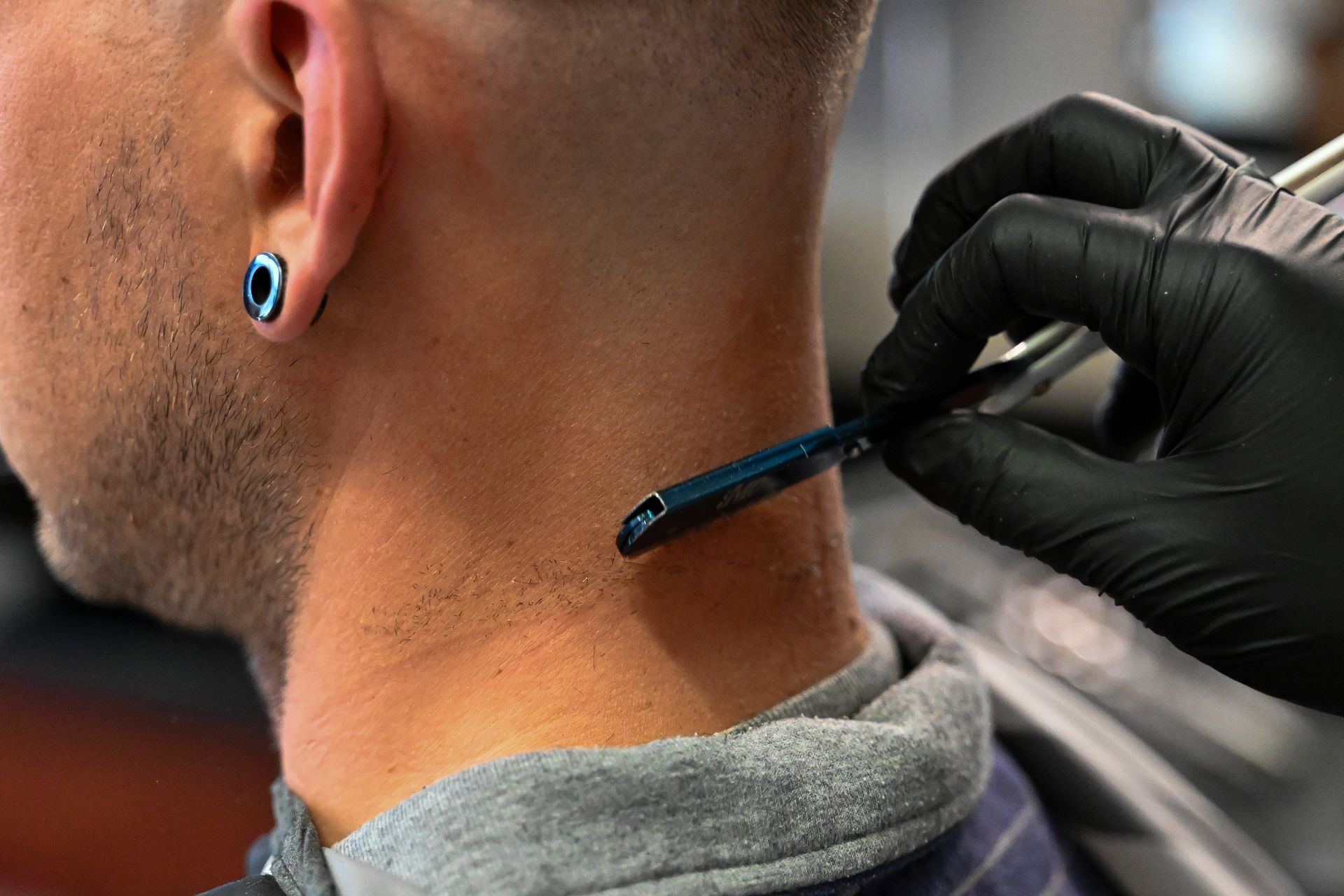 A man is getting his hair cut by a barber with a razor.