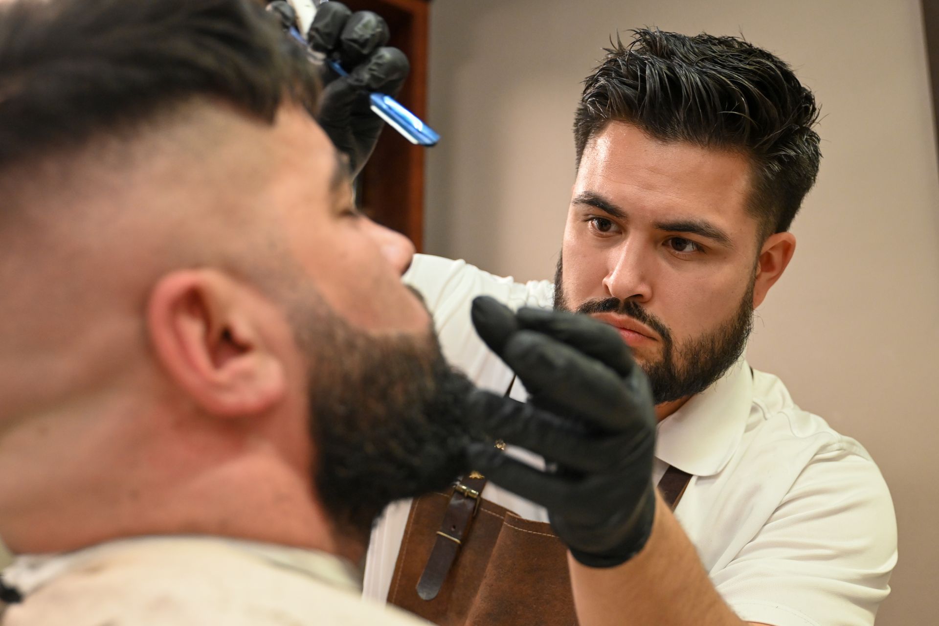 A barber is cutting a man 's beard with a razor.