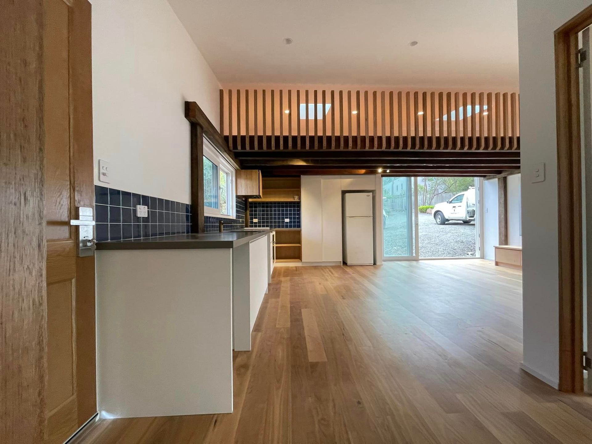 Interior view of a modern kitchen with wooden floors, white cabinets, and a loft above.