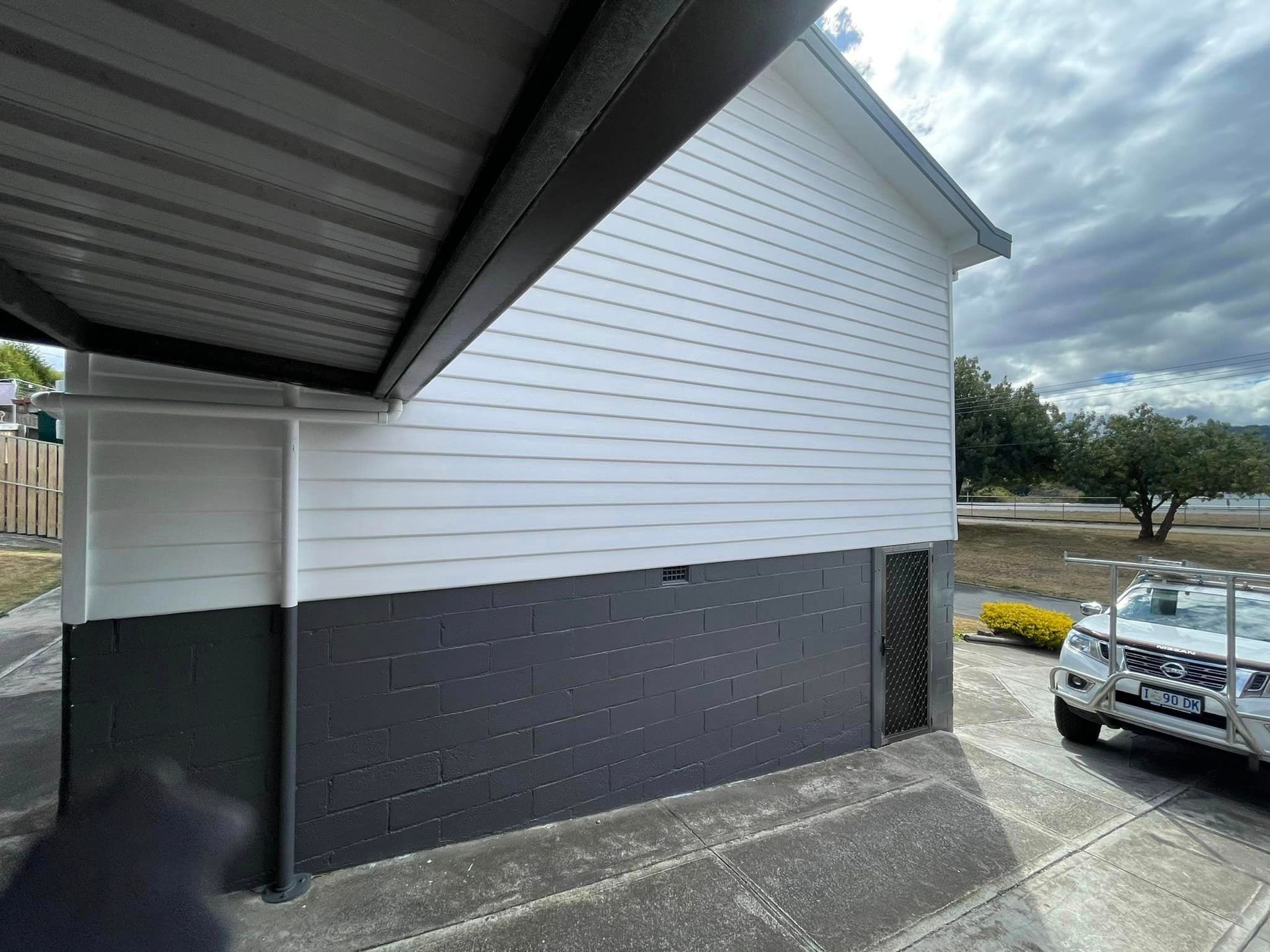 Two-tone house with black brick base and white siding, under a gray roof and next to a driveway and a parked SUV.