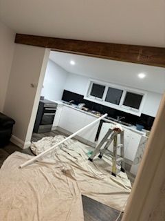 Kitchen under renovation. White cabinets, black backsplash, painter's tarp, ladder, and a long white pipe.
