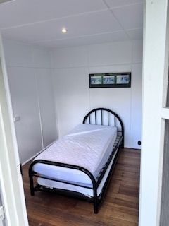 Small white-walled bedroom with a black metal bed, a mattress, and a framed picture above it.