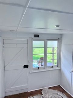 White interior with door, window, and ceiling panels. The window overlooks green foliage.