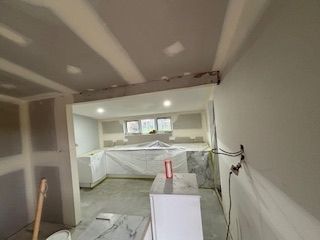 Kitchen under construction, drywall and cabinetry installed. White, gray, and concrete elements visible.