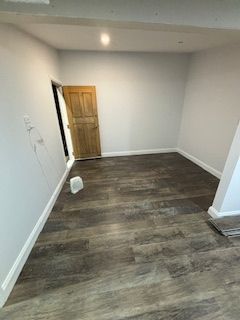 Empty room with dark wood-look flooring, light gray walls, and a wooden door.