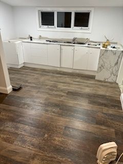 Renovated room with dark wood flooring, white cabinets, and a marble countertop.