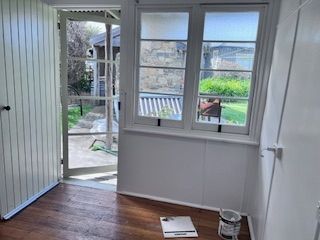 Interior room with open door to a yard, white walls, wooden floor, windows.