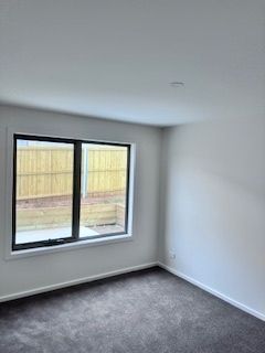 Empty room with dark carpet, white walls, and a window overlooking a wooden fence.
