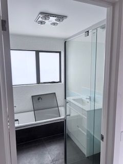 Bathroom with glass shower, white sink cabinet, black tub, and small window.