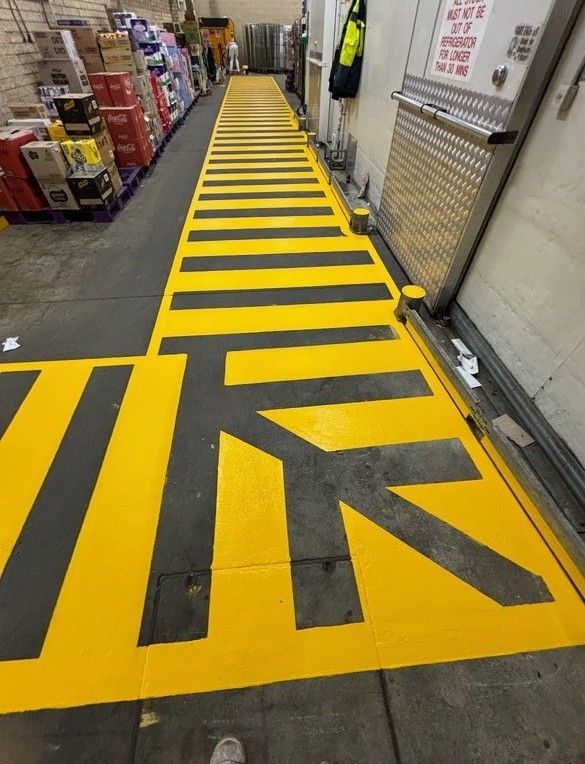 Yellow and black striped floor markings in a warehouse, directing traffic toward a loading door.