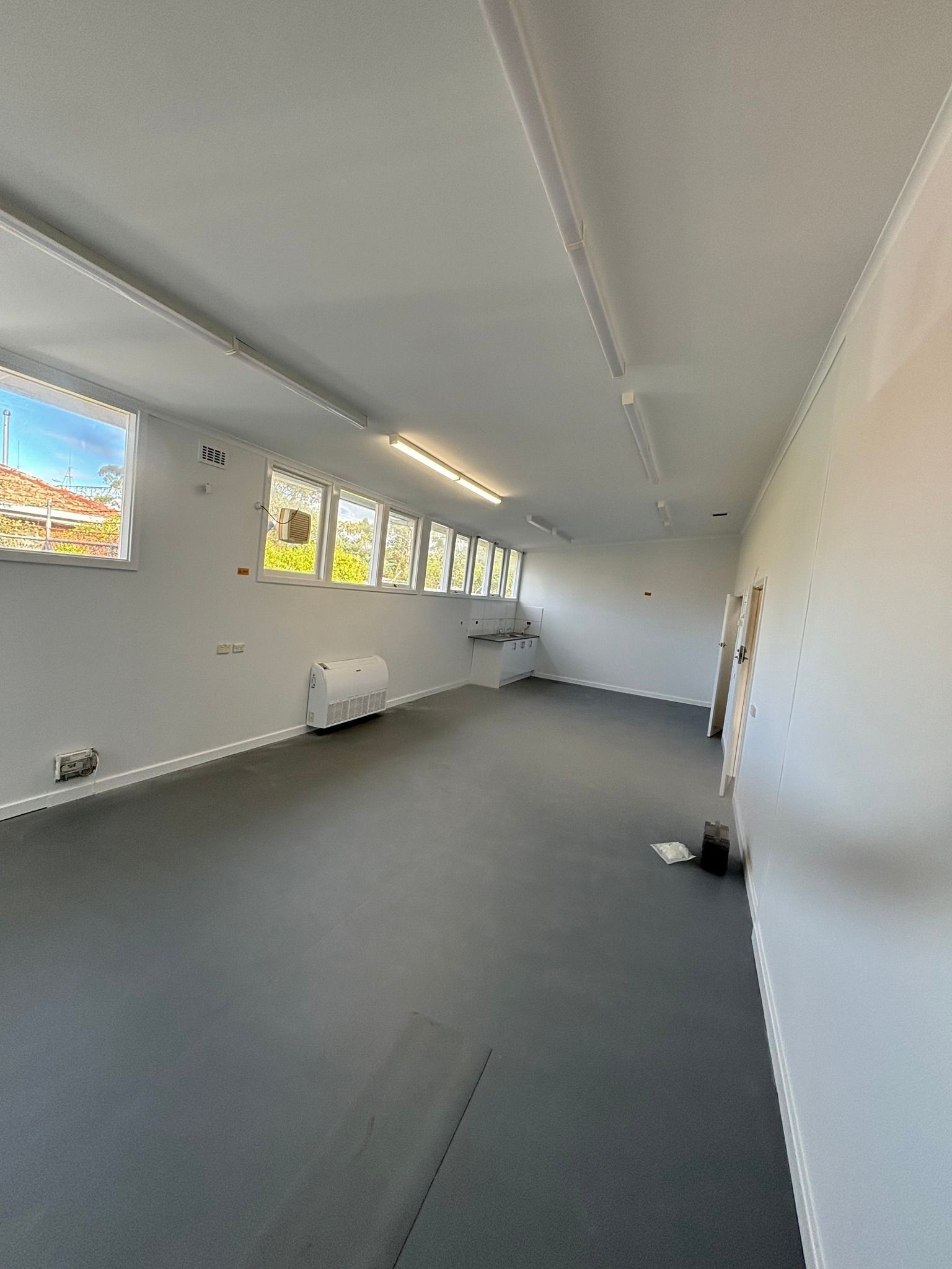 Empty interior with gray floor, white walls, and windows along one side.