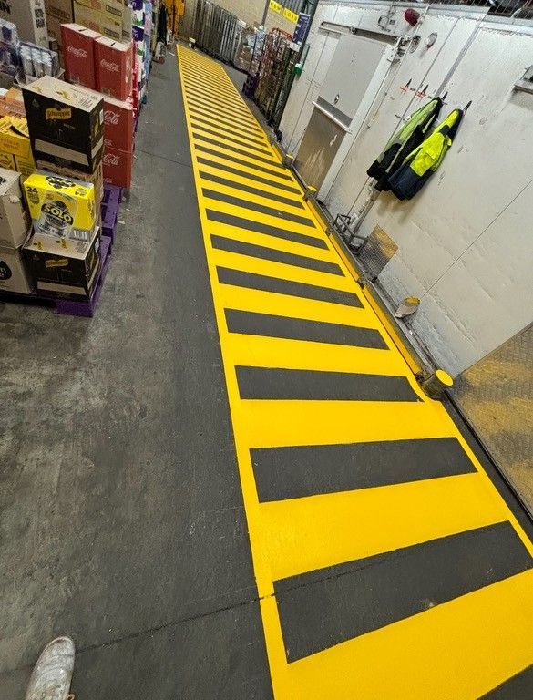 Yellow and black striped floor in a store, leading to a doorway. Pallets of goods are visible nearby.