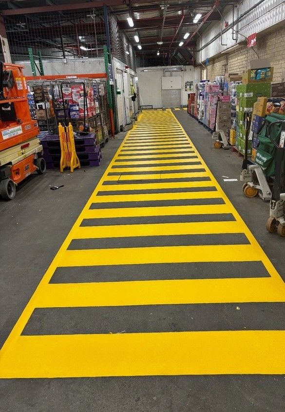 Yellow and black striped floor marking in a warehouse, likely indicating a crosswalk or high-traffic area.