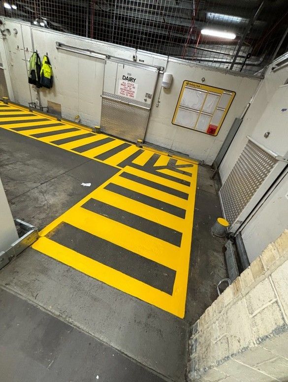 Yellow and black striped floor markings in a loading dock area; a door, and a safety vest are visible.