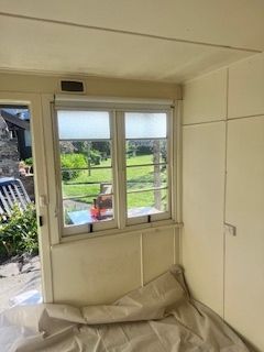 Interior view: Window with white frame, light streaming in, garden visible, beige walls.