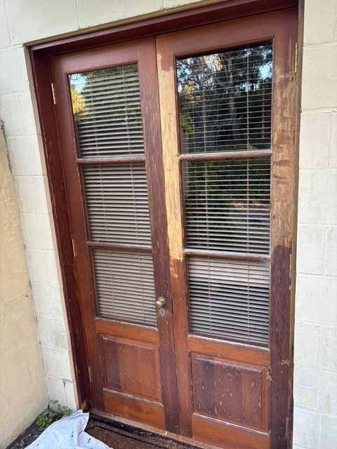 Double wooden doors with glass panes and blinds, showing signs of wear.