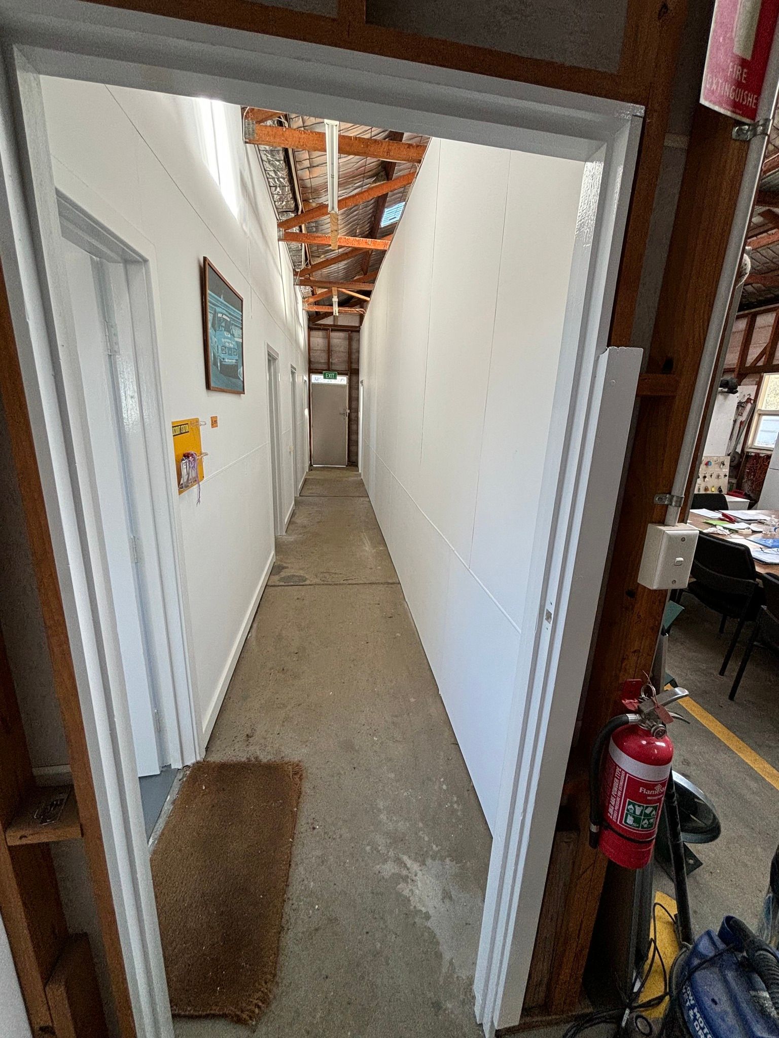 Narrow hallway with white walls and doors, concrete floor, open ceiling.