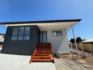 Modern house with dark grey and white siding, wooden stairs, and a clear blue sky.