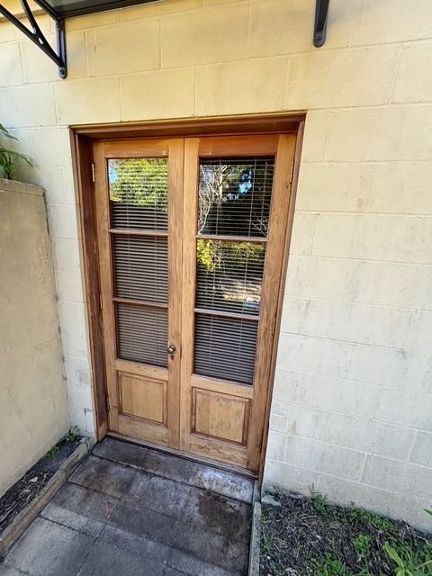 Double wooden doors with glass panes and blinds set in a light stone wall.