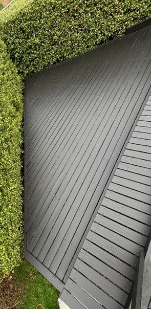 A grey slat roof next to a dense green hedge and grass.
