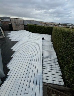 Partially painted white wooden deck surrounded by green hedges and a cloudy sky.