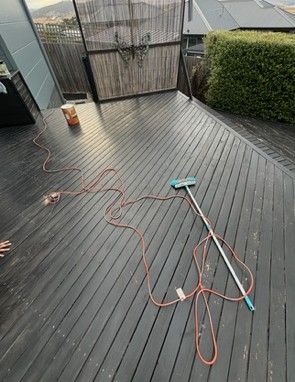Wooden deck with a long orange extension cord and a cleaning brush lying on it.