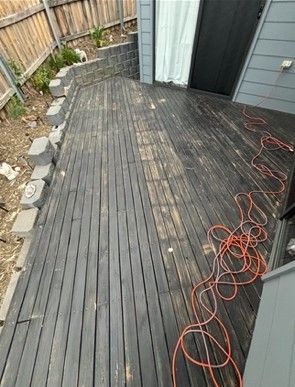 Wooden deck with peeling black stain, orange extension cord, and door to a house.