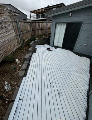 Gray deck next to a gray house, with a wooden fence and a small garden.
