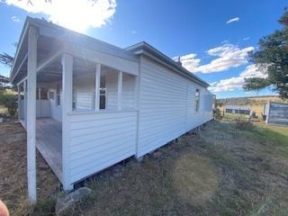White, weathered house with a porch under a blue sky with clouds.