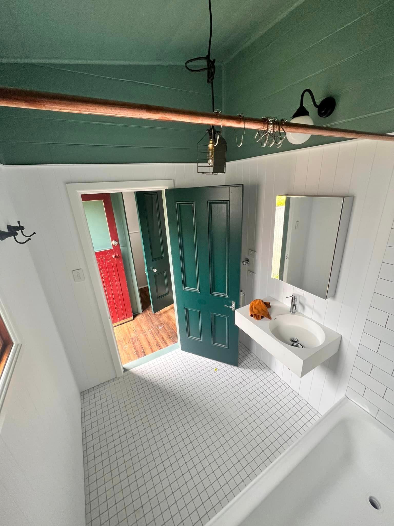 Bathroom with white and gray tiled floor, green door and ceiling, and a sink.