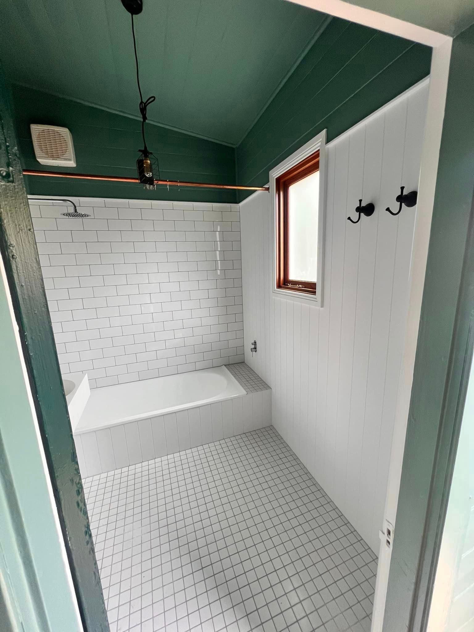 Small bathroom with white tiled walls and floor, green ceiling. Includes a bathtub, shower, and window.