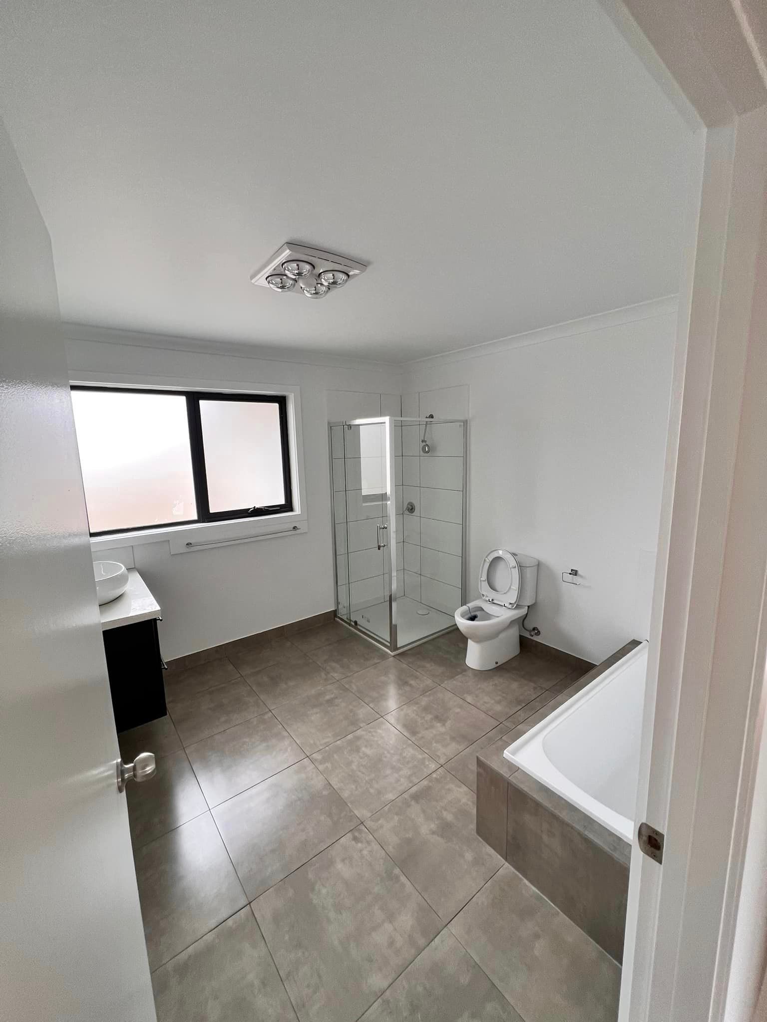 Modern bathroom with tiled floor, white walls, and glass shower. Features toilet, vanity, and bathtub.