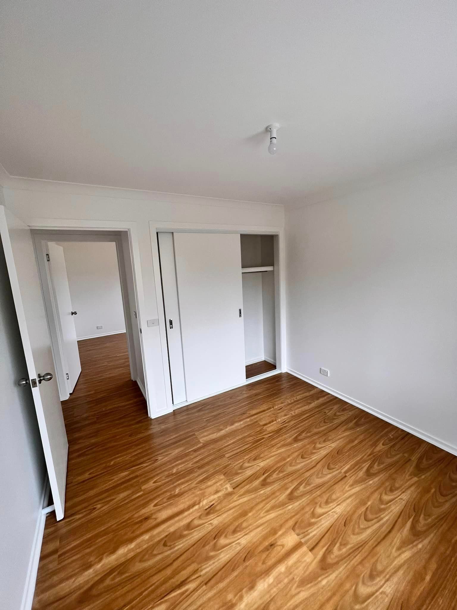 Empty bedroom with wooden floor, white walls, and a closet with sliding doors.