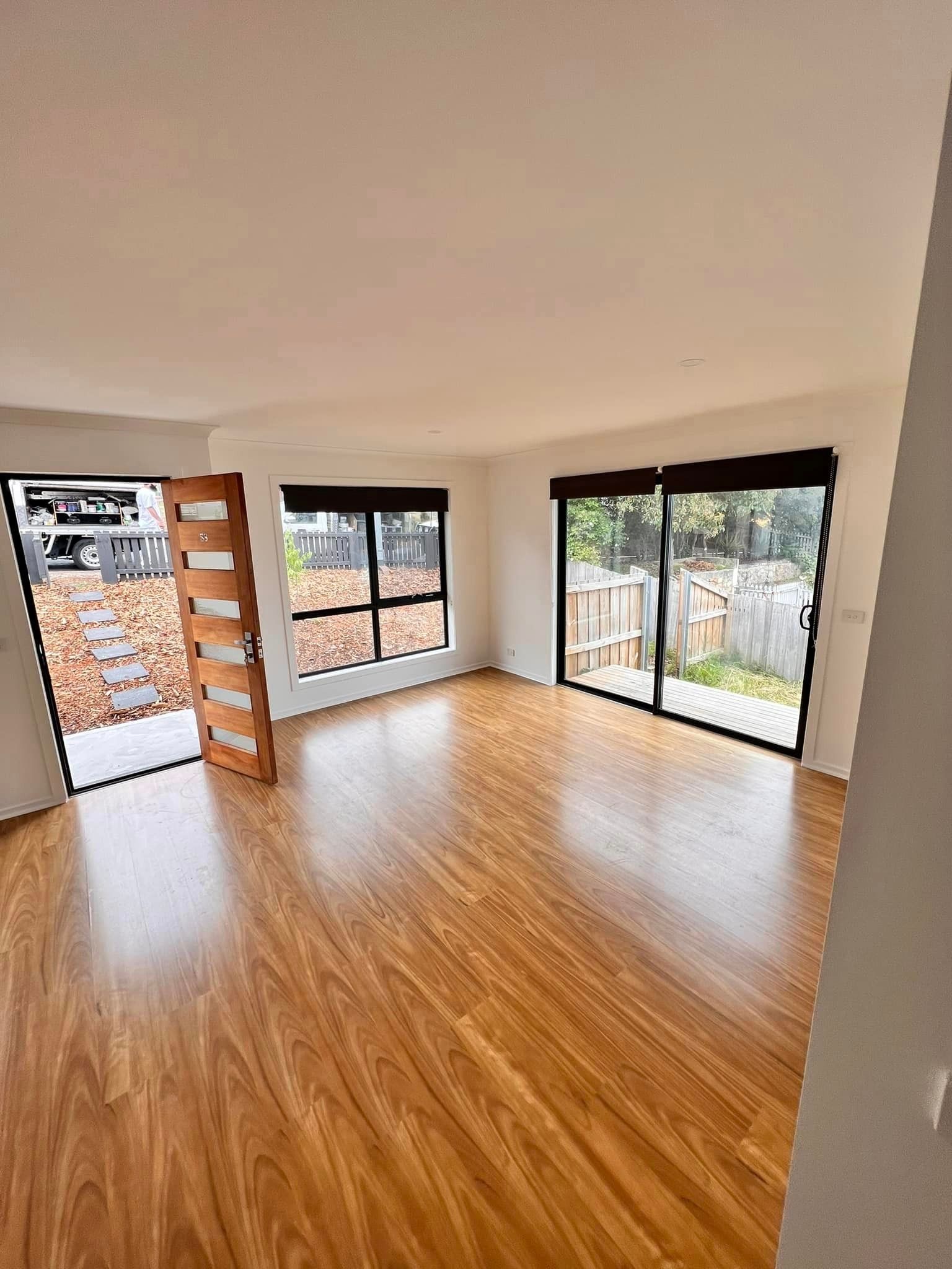 Empty room with wooden floors, large windows, and an open wooden door.