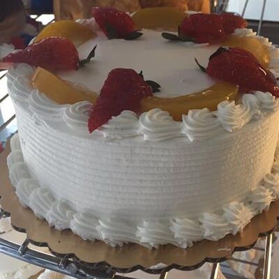 A two tiered cake with pink frosting and fruit on top.