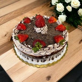 A chocolate cake with strawberries on top is sitting on a wooden table.