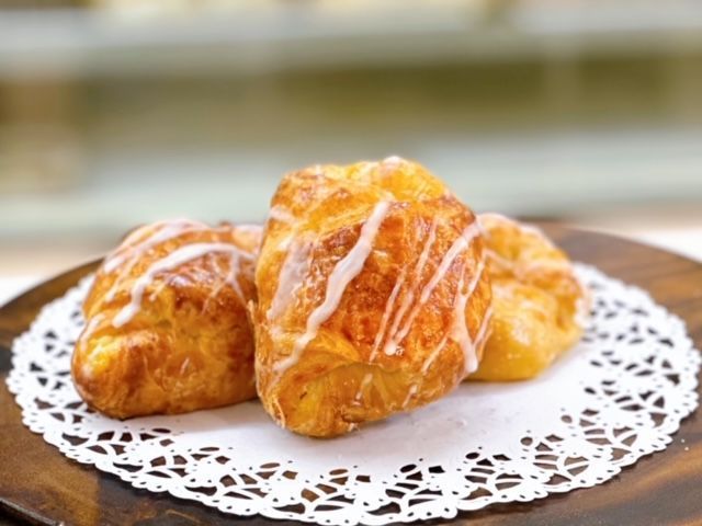 Three pastries are sitting on a white lace napkin on a wooden table.