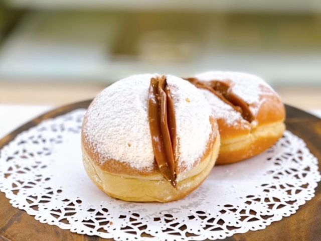 Two donuts covered in powdered sugar are sitting on a wooden cutting board.