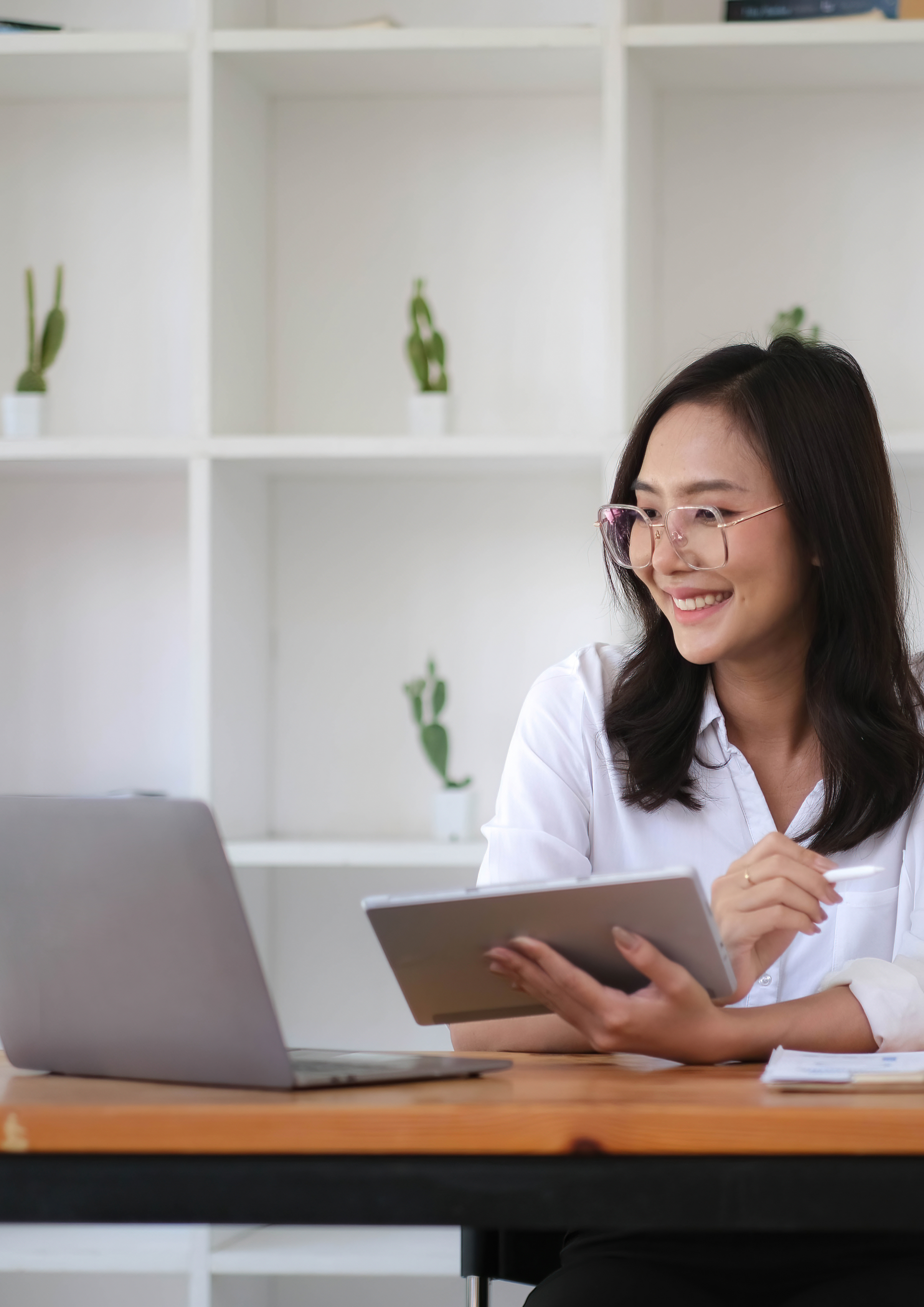 A woman is sitting at a desk with a laptop and a tablet.