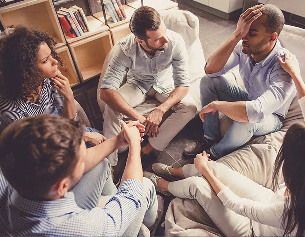 A group of people are sitting in a circle holding hands.