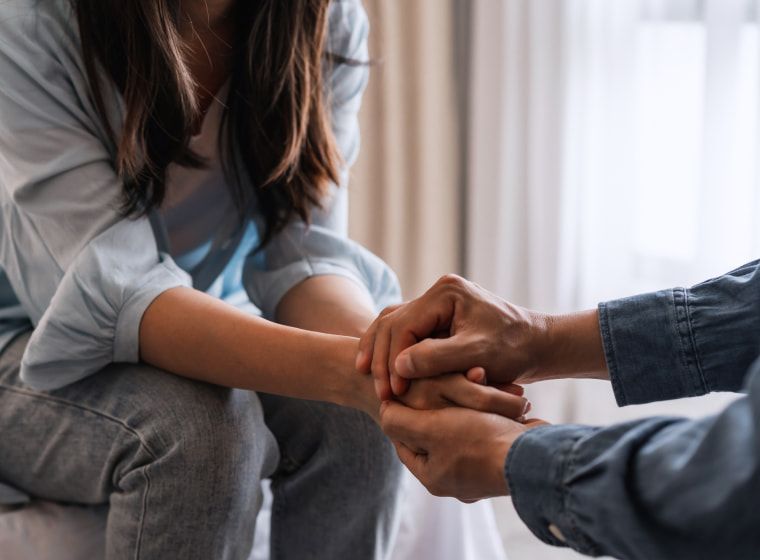 A man is holding a woman 's hand while sitting on a couch.
