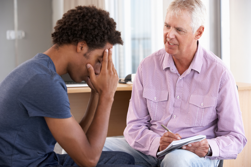 A man is talking to a young man who is covering his face.
