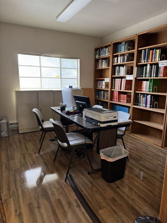A room with a desk , chairs , shelves and a window.