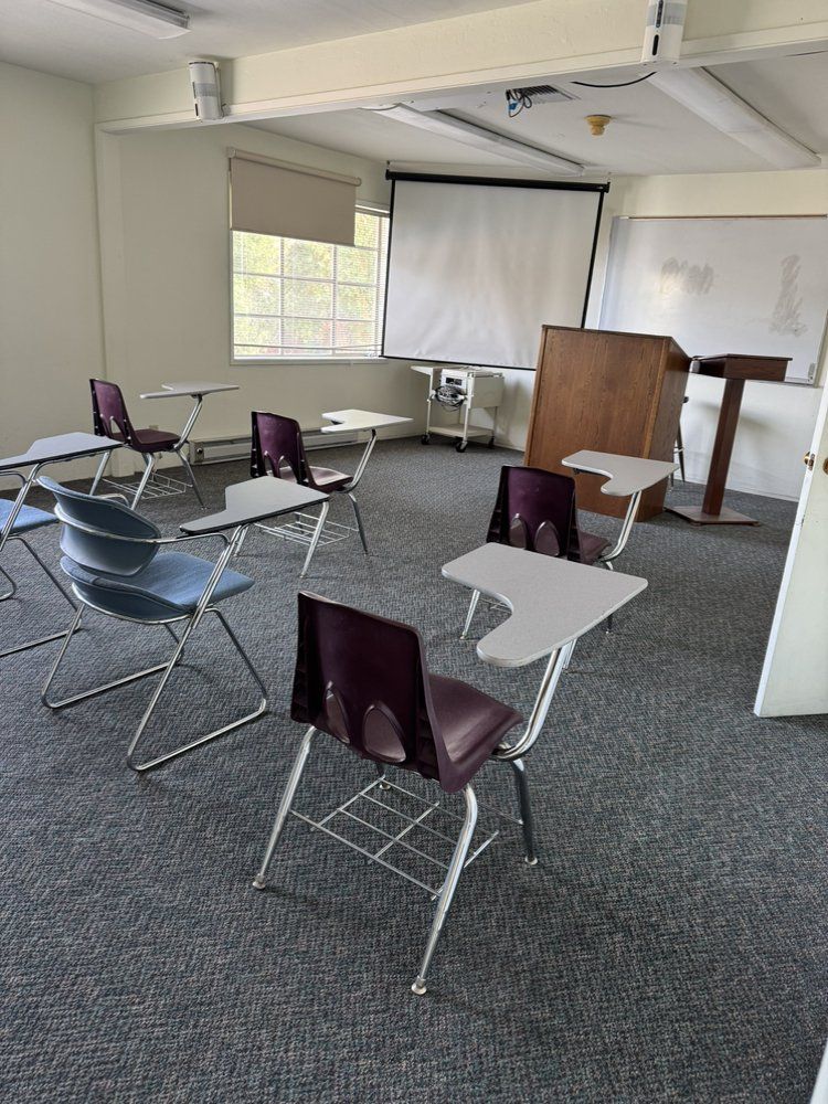 A classroom with desks and chairs and a projector screen.
