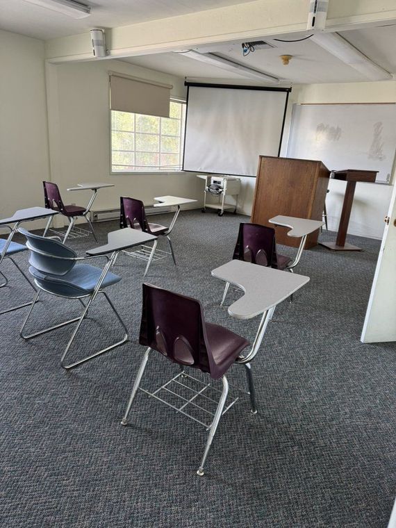 A classroom with desks and chairs and a projector screen.