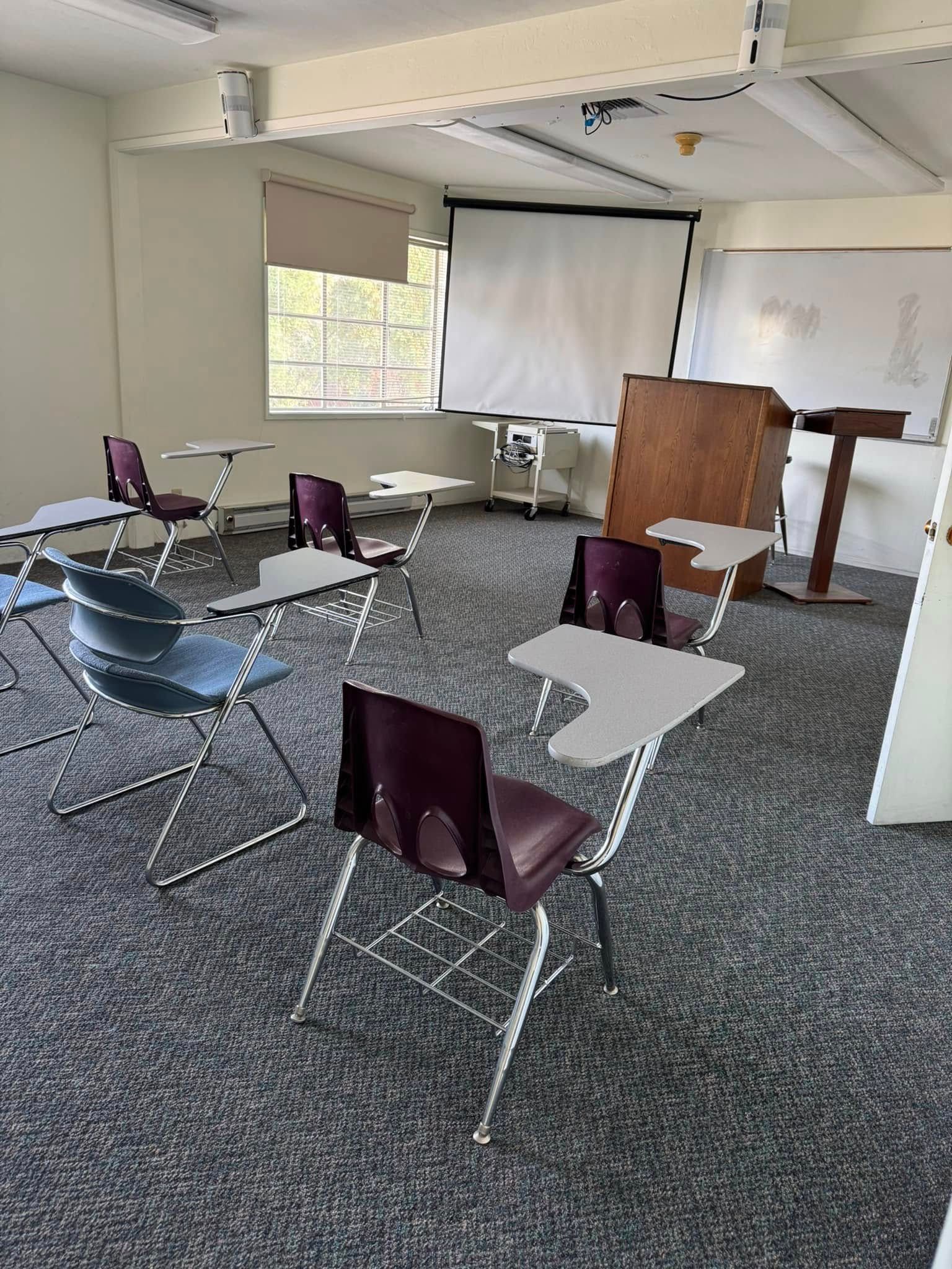 A classroom with desks and chairs and a projector screen.